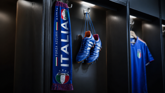 Écharpe de supporter Italie et paire de crampons suspendus dans un vestiaire professionnel sombre, visuel dramatique sur l’absence de l’Italie à la Coupe du Monde 2026.
